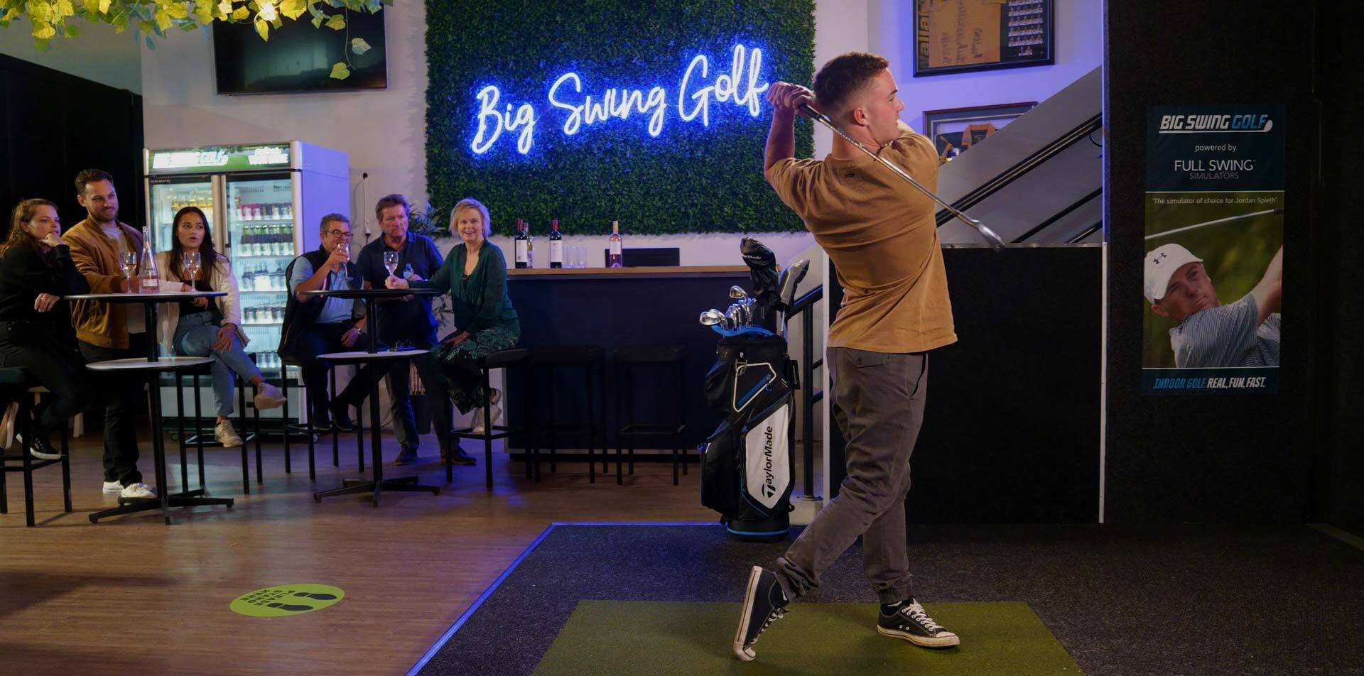 Big Swing Golf - golfer swinging a golf club with neon sign behind saying "Big Swing Golf" as friends watch on