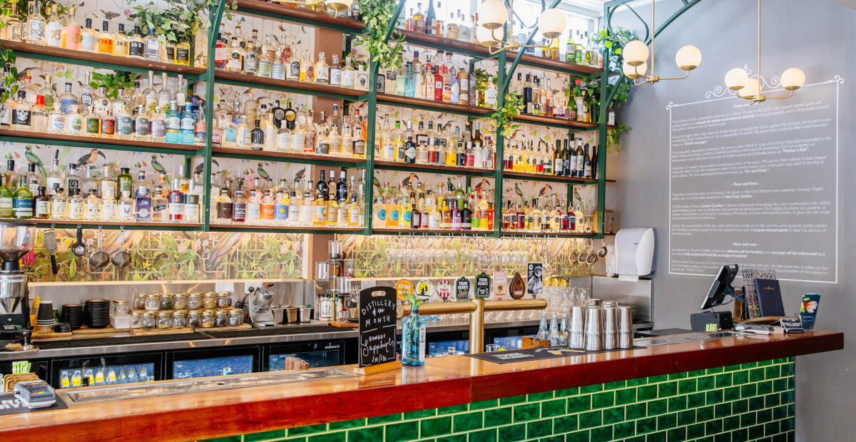 Covent Garden West End image showing a bar with green tiles and a red top with hundreds of spirit bottles behind to order from