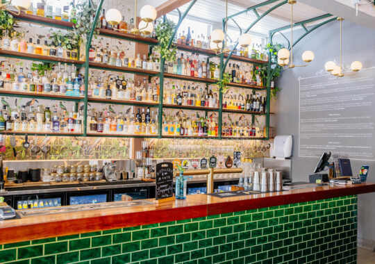 Covent Garden West End image showing a bar with green tiles and a red top with hundreds of spirit bottles behind to order from